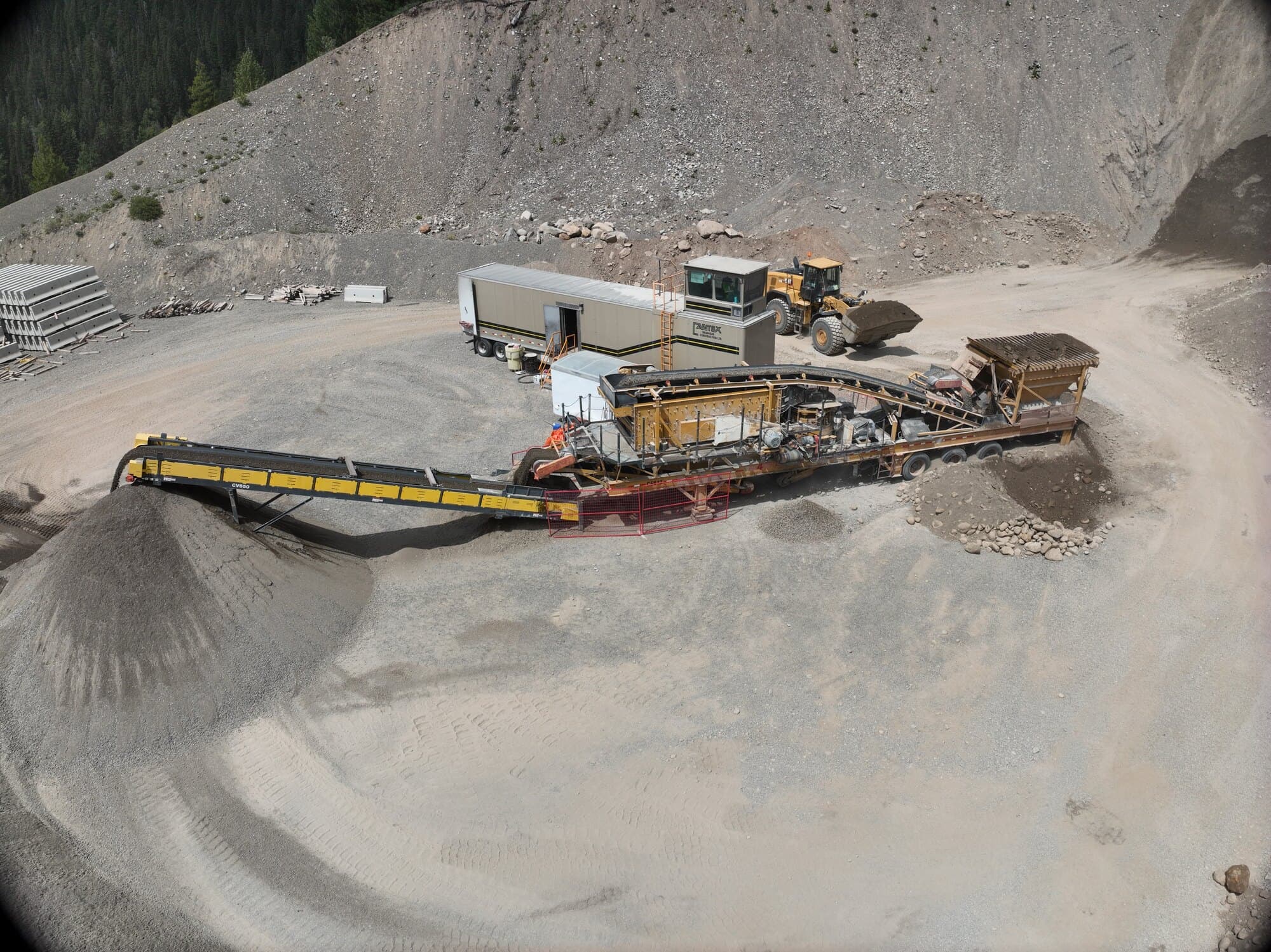 A Cantex screening plant and stacking conveyor working below a high rock face, stockpiles building at the end of the belt.